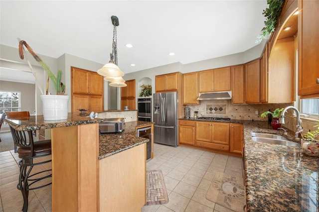 kitchen featuring a kitchen breakfast bar, sink, dark stone countertops, a kitchen island, and stainless steel appliances