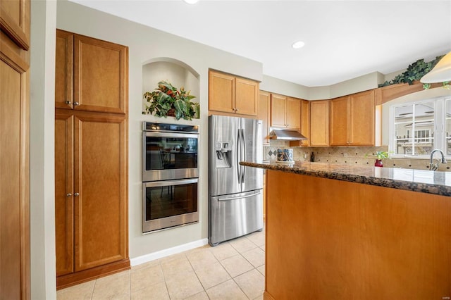 kitchen featuring dark stone counters, sink, light tile patterned floors, appliances with stainless steel finishes, and tasteful backsplash