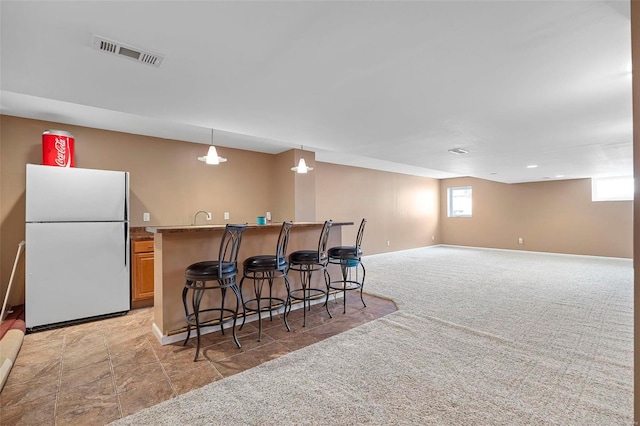 kitchen with hanging light fixtures, white fridge, light colored carpet, a breakfast bar area, and light brown cabinetry