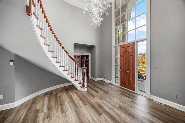 foyer entrance featuring a high ceiling, wood-type flooring, crown molding, and a notable chandelier