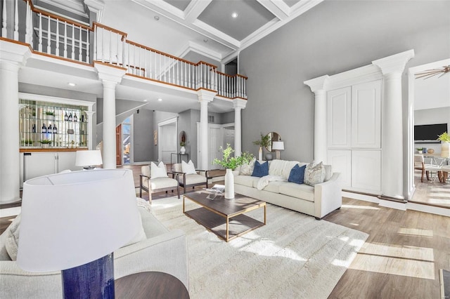 living room featuring light hardwood / wood-style flooring, beam ceiling, a high ceiling, coffered ceiling, and decorative columns