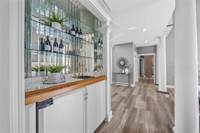 bar featuring sink, light hardwood / wood-style flooring, ornate columns, and butcher block countertops