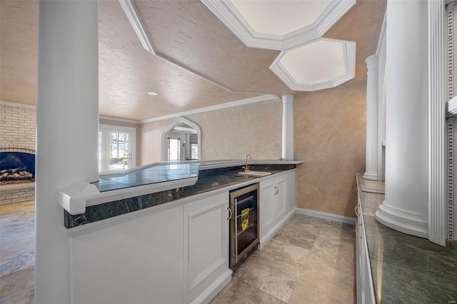 kitchen featuring crown molding, ornate columns, sink, white cabinetry, and beverage cooler