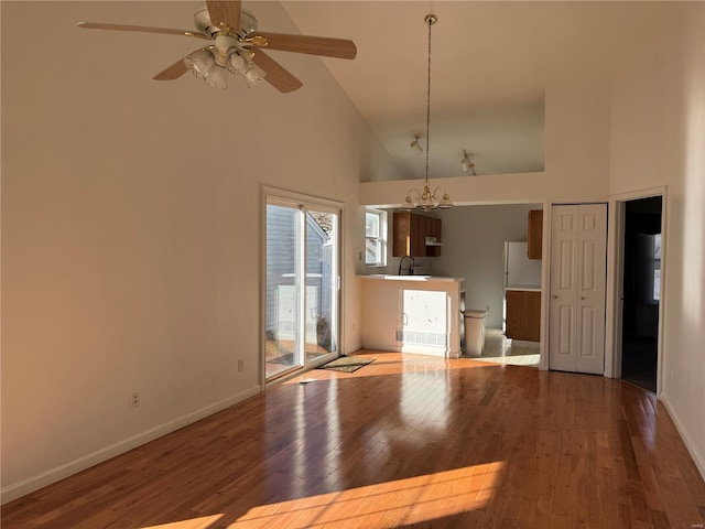 unfurnished dining area with wood-type flooring, ceiling fan with notable chandelier, and high vaulted ceiling