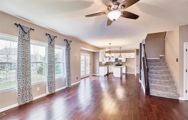 unfurnished living room with ceiling fan with notable chandelier, a healthy amount of sunlight, and dark hardwood / wood-style flooring