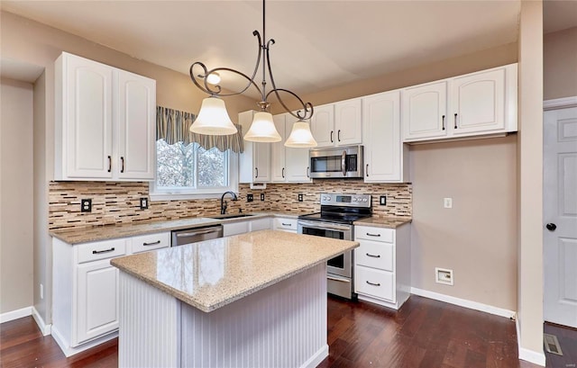 kitchen with a center island, hanging light fixtures, light stone countertops, white cabinetry, and stainless steel appliances