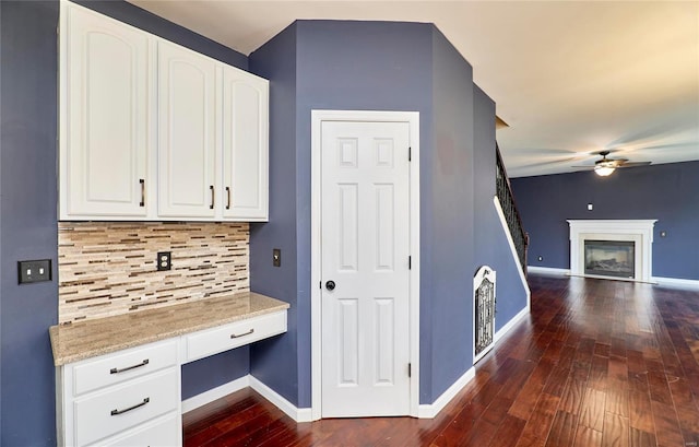 kitchen featuring tasteful backsplash, light stone counters, ceiling fan, built in desk, and white cabinetry