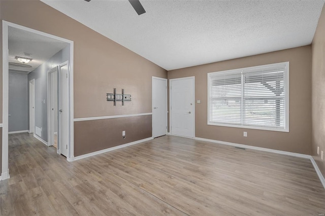 empty room featuring ceiling fan, light hardwood / wood-style floors, lofted ceiling, and a textured ceiling