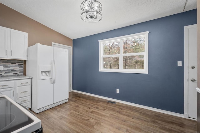 kitchen with decorative backsplash, white refrigerator with ice dispenser, decorative light fixtures, white cabinets, and lofted ceiling