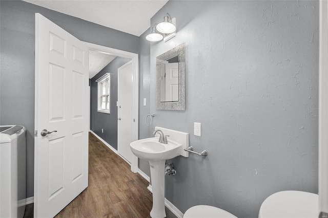 bathroom with wood-type flooring, a textured ceiling, toilet, and washing machine and clothes dryer