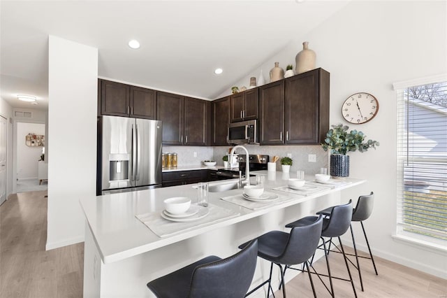 kitchen featuring kitchen peninsula, light wood-type flooring, tasteful backsplash, a breakfast bar, and stainless steel appliances