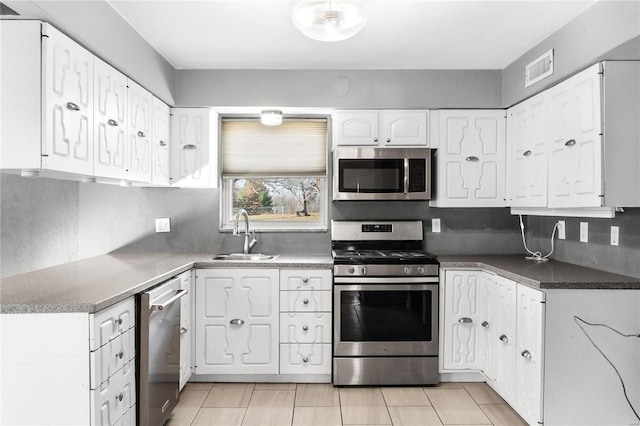 kitchen featuring stainless steel appliances, tasteful backsplash, light tile patterned flooring, white cabinets, and sink