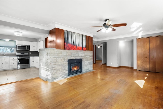 unfurnished living room featuring light hardwood / wood-style floors, a stone fireplace, ceiling fan, crown molding, and sink