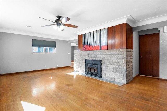 unfurnished living room with ceiling fan, a wood stove, ornamental molding, and light hardwood / wood-style floors