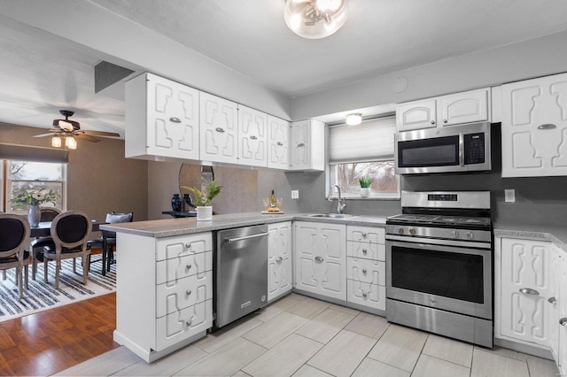 kitchen with appliances with stainless steel finishes, sink, white cabinets, ceiling fan, and kitchen peninsula