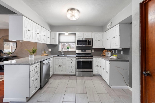 kitchen with appliances with stainless steel finishes, kitchen peninsula, sink, and white cabinets