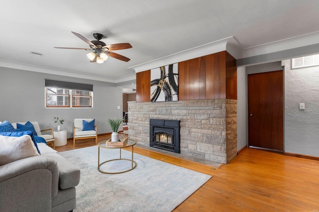 living room with ceiling fan, crown molding, a fireplace, and light hardwood / wood-style flooring