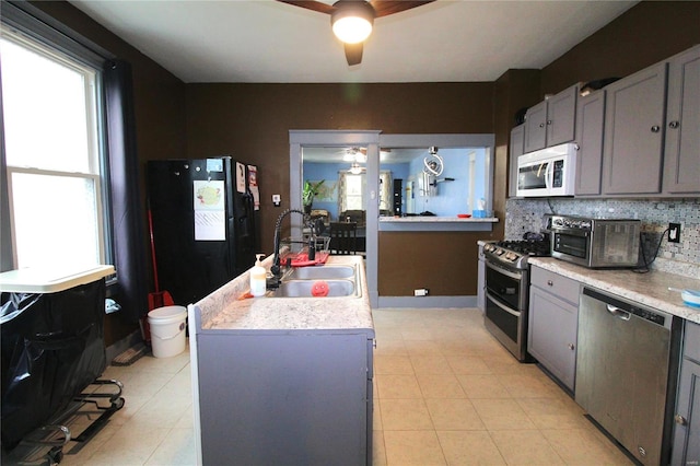 kitchen with sink, stainless steel appliances, an island with sink, gray cabinets, and decorative backsplash