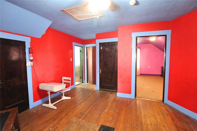 unfurnished bedroom with a textured ceiling, wood-type flooring, and lofted ceiling