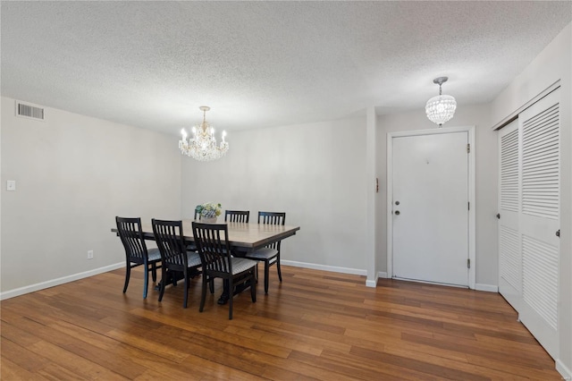 dining area with a textured ceiling, hardwood / wood-style flooring, and an inviting chandelier