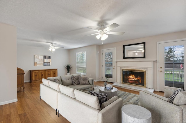 living room with ceiling fan, a textured ceiling, and light hardwood / wood-style flooring