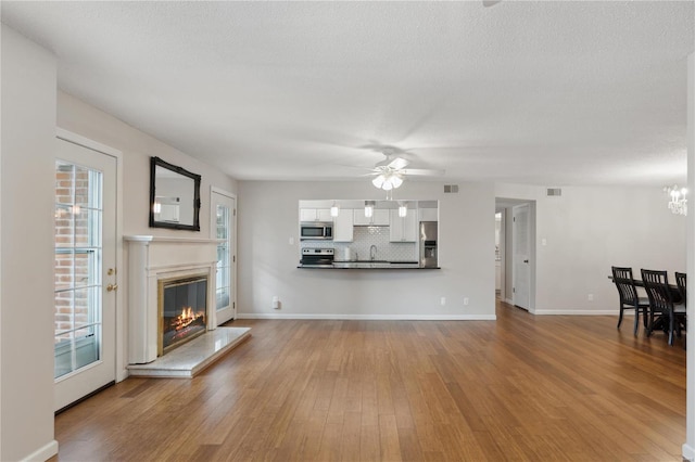 unfurnished living room featuring wood-type flooring, ceiling fan with notable chandelier, a textured ceiling, and sink