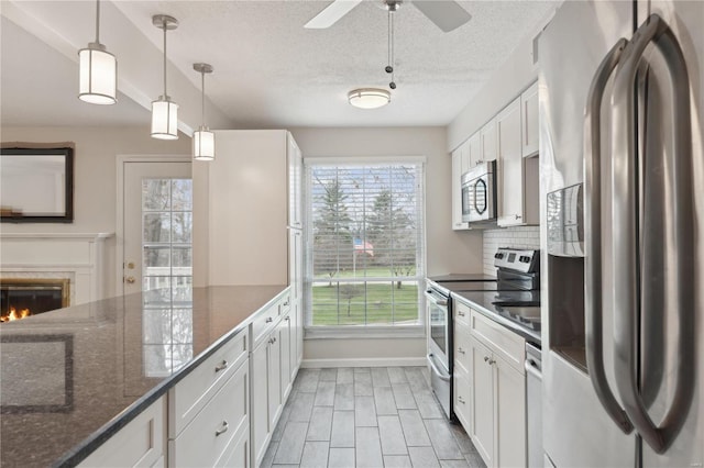 kitchen with stainless steel appliances, a healthy amount of sunlight, decorative light fixtures, dark stone countertops, and white cabinets