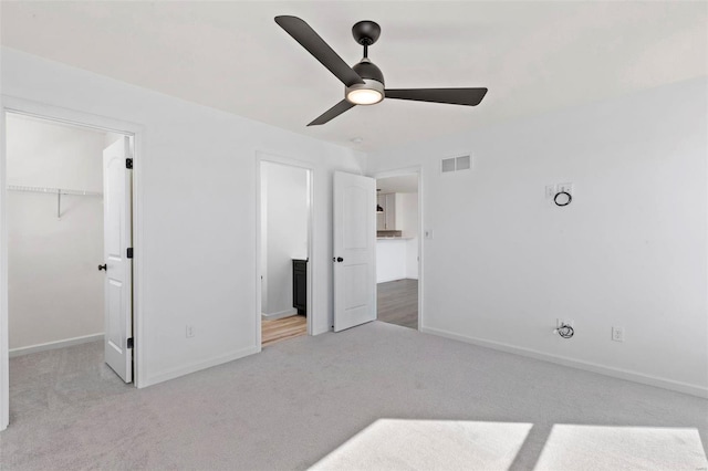 unfurnished bedroom with a walk in closet, ceiling fan, a closet, and light colored carpet