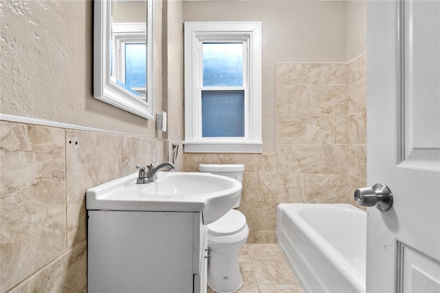 bathroom with a washtub, vanity, toilet, and tile walls