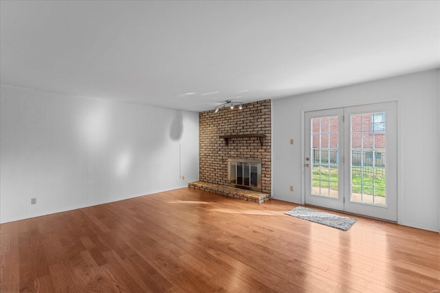 unfurnished living room with plenty of natural light, ceiling fan, light wood-type flooring, and a brick fireplace