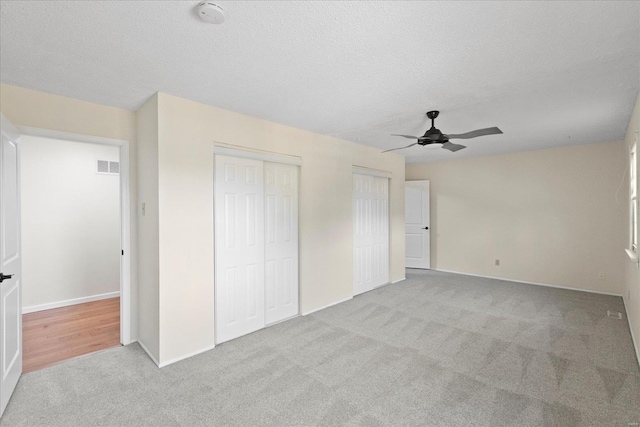 unfurnished bedroom featuring two closets, ceiling fan, light carpet, and a textured ceiling