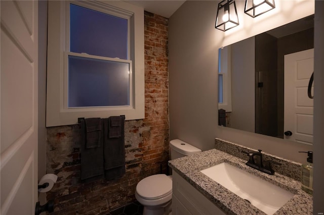 bathroom featuring vanity, brick wall, and toilet