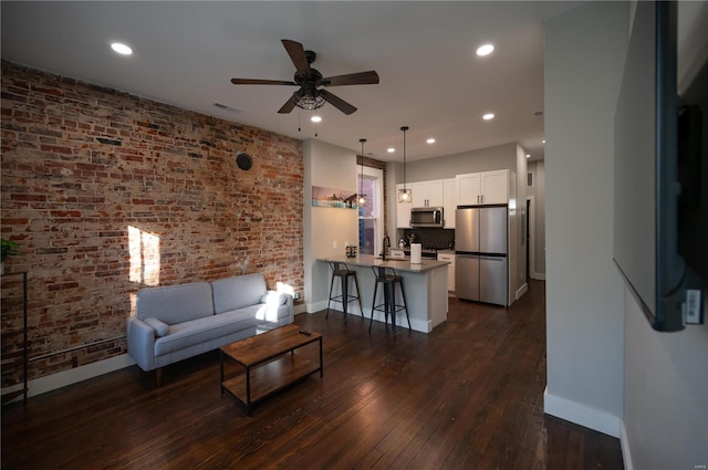 living room with ceiling fan, dark wood-type flooring, and brick wall