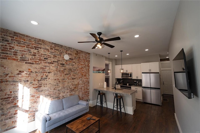 living room with brick wall, dark hardwood / wood-style floors, ceiling fan, and sink