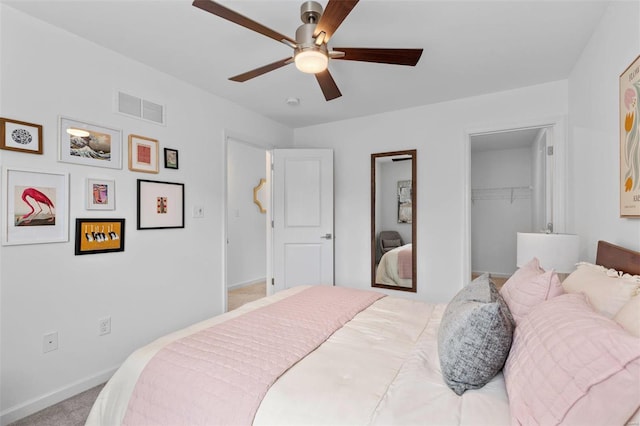 bedroom featuring light carpet, a walk in closet, a closet, and ceiling fan