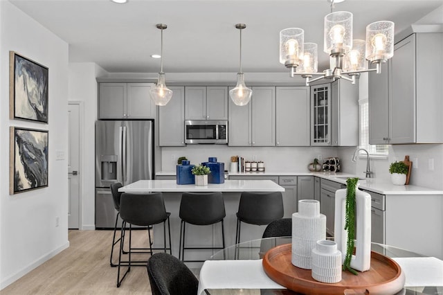 kitchen featuring gray cabinetry, sink, stainless steel appliances, light hardwood / wood-style flooring, and decorative light fixtures