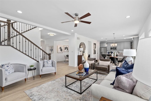 living room with ceiling fan with notable chandelier and light hardwood / wood-style floors