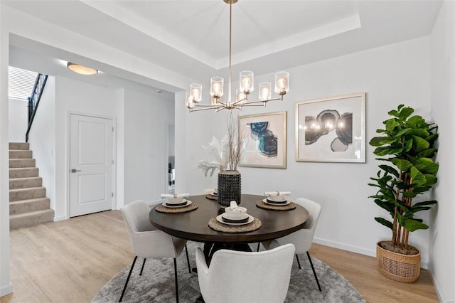 dining space featuring a raised ceiling, an inviting chandelier, and light hardwood / wood-style flooring