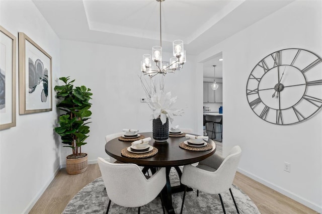 dining room with a tray ceiling, light hardwood / wood-style floors, and an inviting chandelier