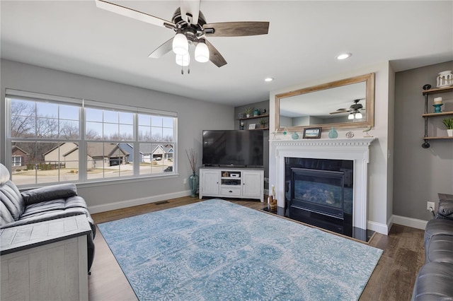 living area featuring a fireplace with flush hearth, wood finished floors, visible vents, and baseboards