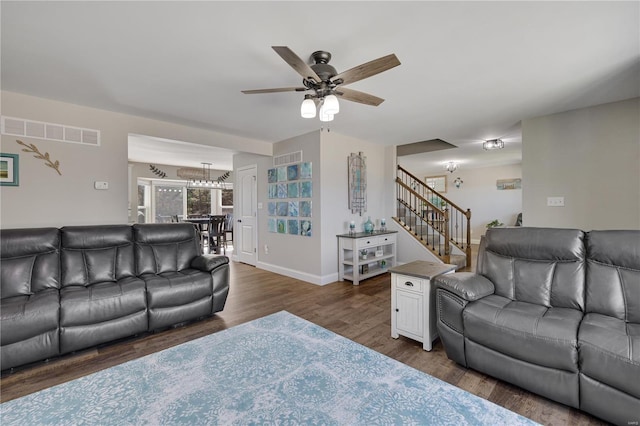 living area featuring dark wood-style flooring, a ceiling fan, visible vents, baseboards, and stairway