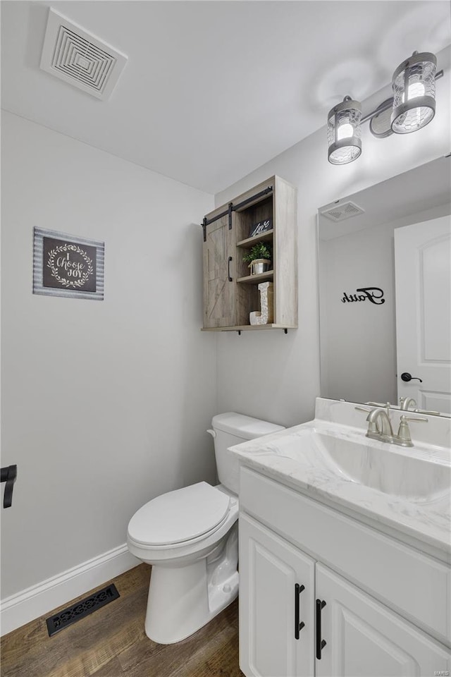 half bathroom with visible vents, vanity, baseboards, and wood finished floors