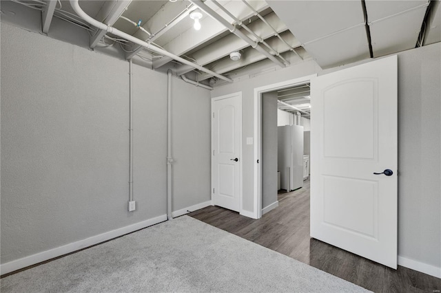 unfinished basement with dark wood-style floors, freestanding refrigerator, and baseboards