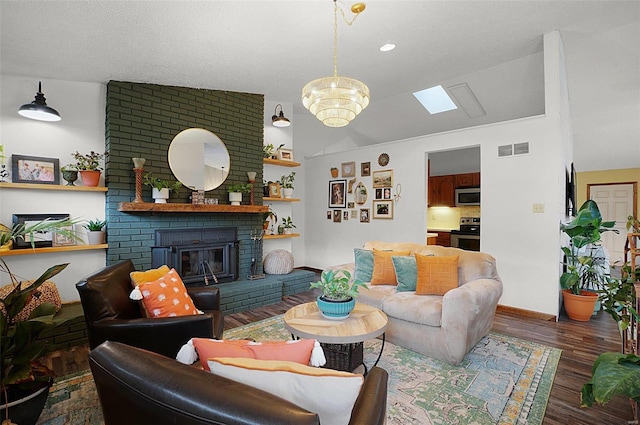 living room with a fireplace, vaulted ceiling with skylight, dark wood-type flooring, and an inviting chandelier