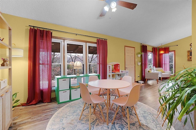 dining space with ceiling fan, light hardwood / wood-style floors, lofted ceiling, and a textured ceiling