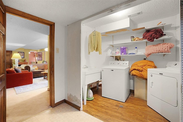 laundry area with washer and dryer, a textured ceiling, and light hardwood / wood-style floors