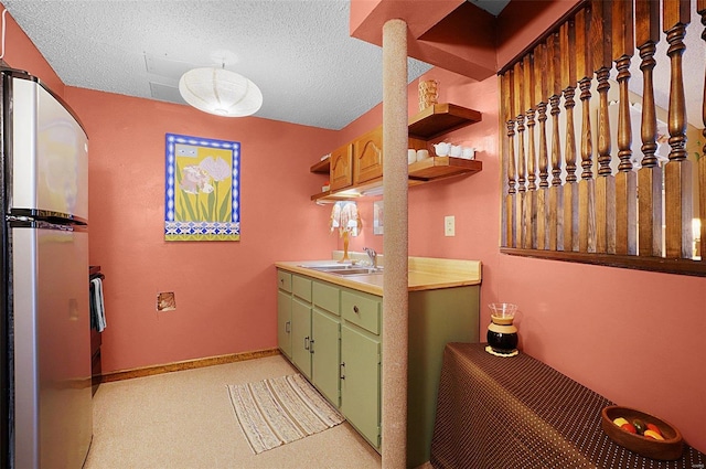 kitchen featuring sink, green cabinets, stainless steel fridge, light colored carpet, and a textured ceiling