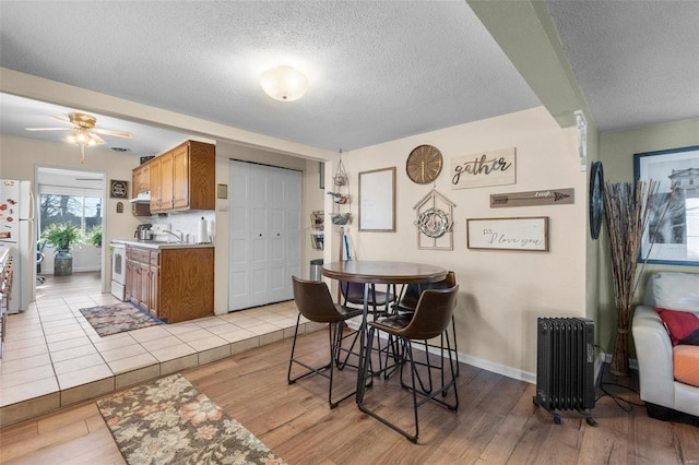 dining area with a textured ceiling, ceiling fan, sink, radiator heating unit, and light hardwood / wood-style floors