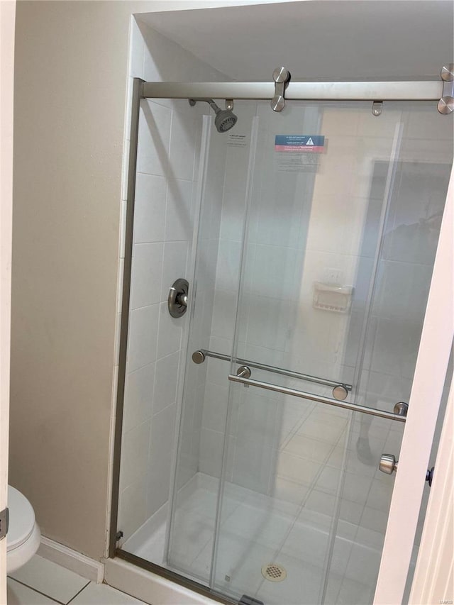 bathroom featuring tile patterned flooring, toilet, and a shower with shower door