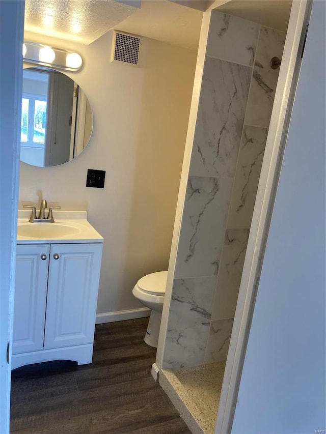 bathroom with a tile shower, wood-type flooring, a textured ceiling, toilet, and vanity